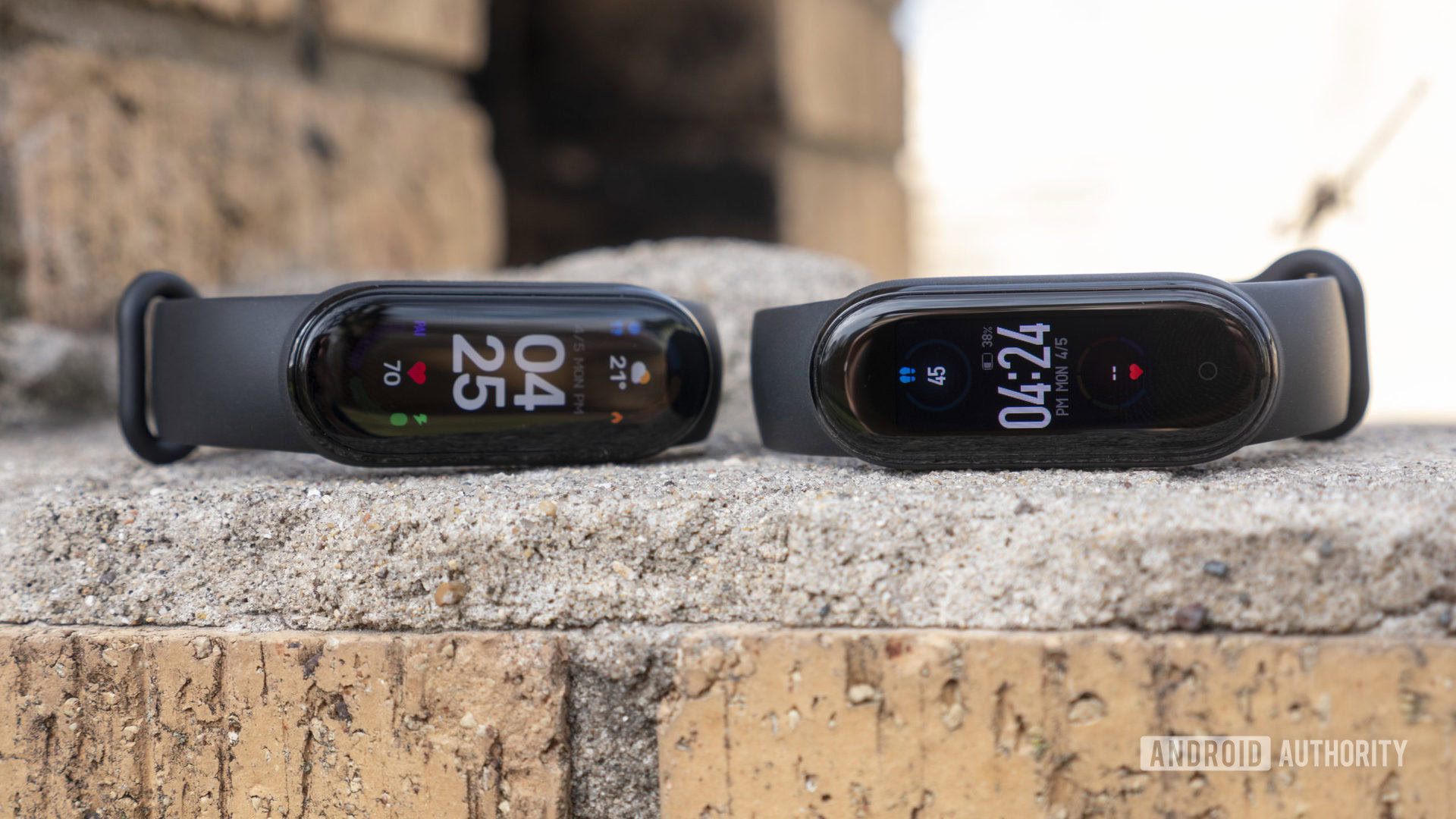 A Xiaomi Mi Band 6 and Xiaomi Mi Band rest side by side on a brick wall.