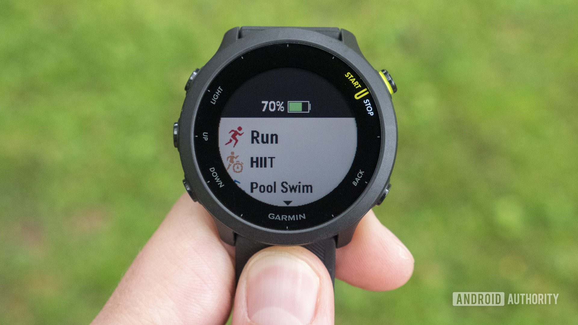 A user holds up a Garmin Forerunner 55 displaying activity profiles.