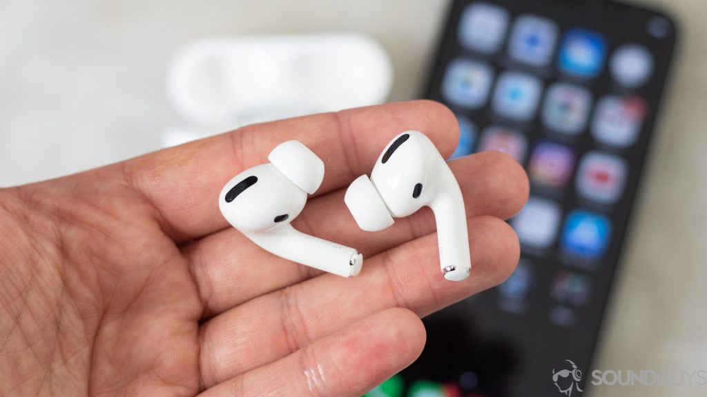 Apple AirPods Pro (1st generation) in hand with an iPhone in the background.