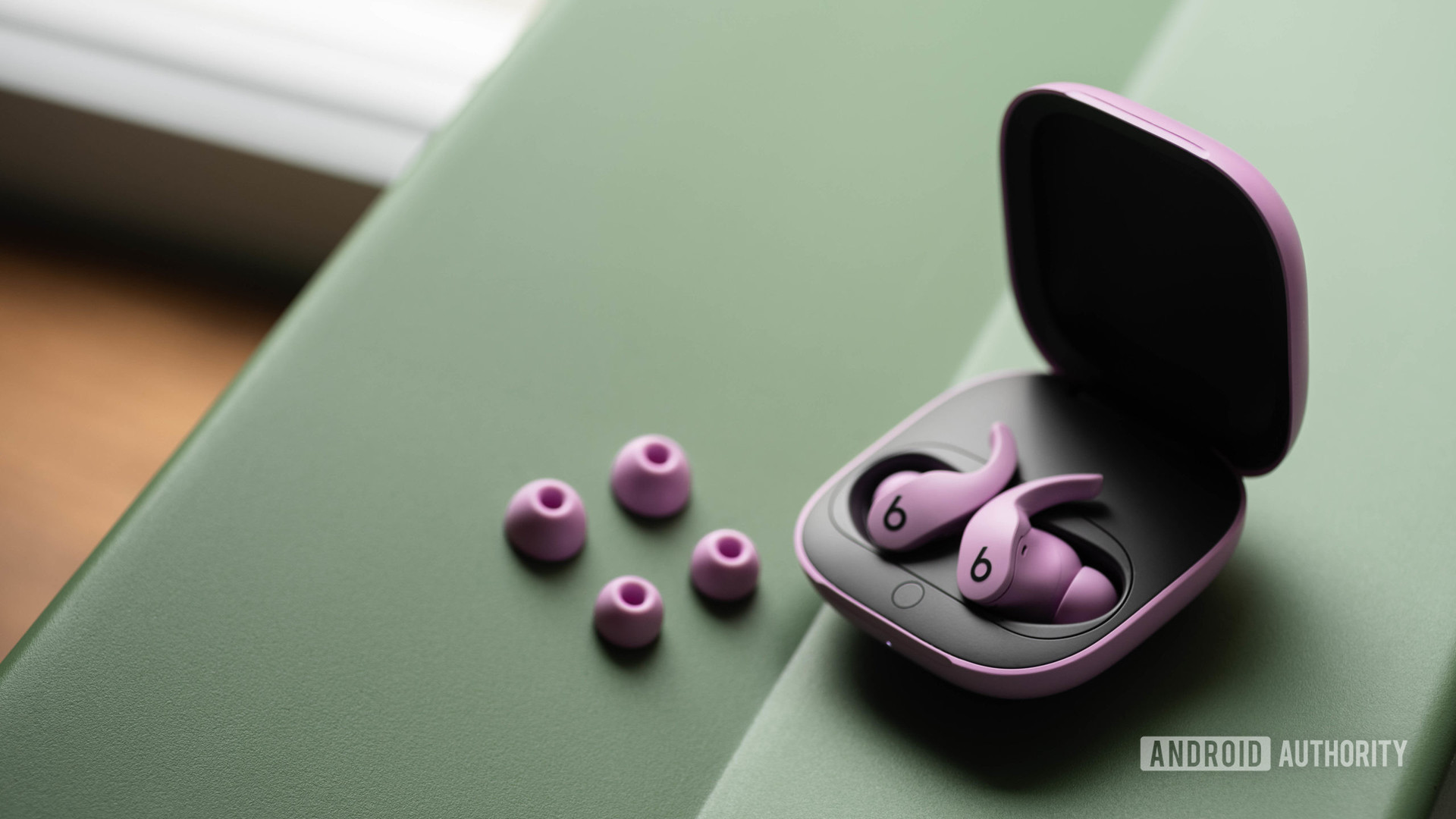 The Beats Fit Pro noise cancelling true wireless earbuds in the open case and next to the two extra pairs of ear tips, all of which are in the purple variant.