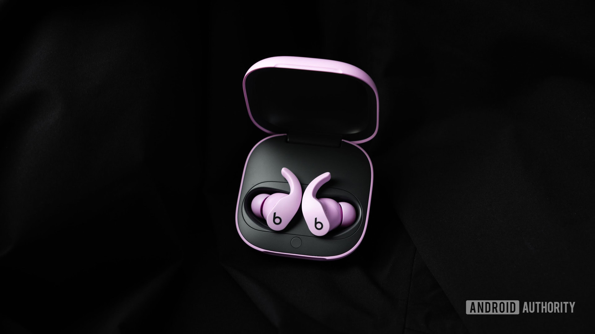 Beats Fit Pro noise canceling true wireless headphones in purple sit in the open charging case on a black cloth background.