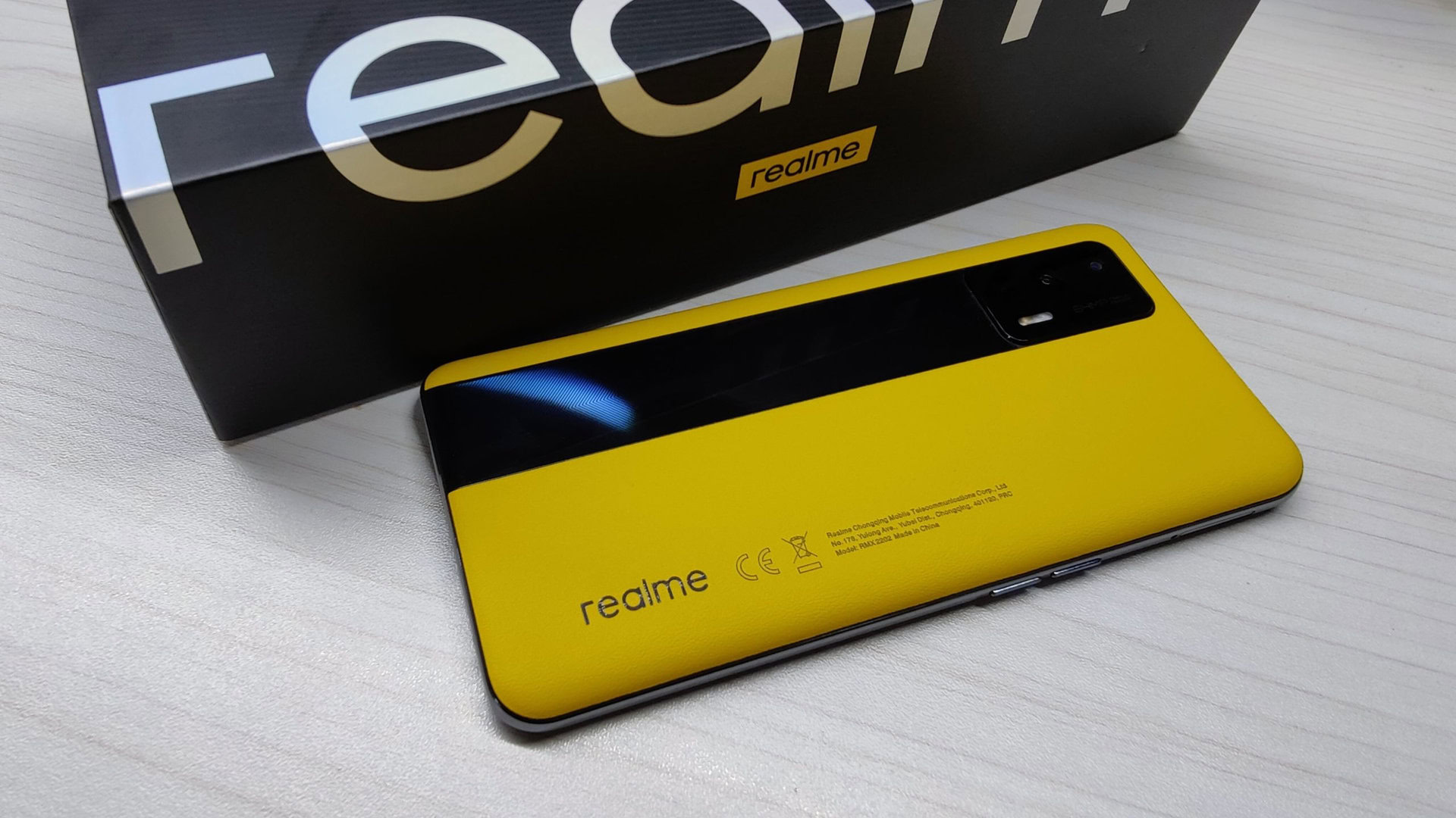 Realme GT Europe in geel naast de verpakking, met achterkant van de telefoon.