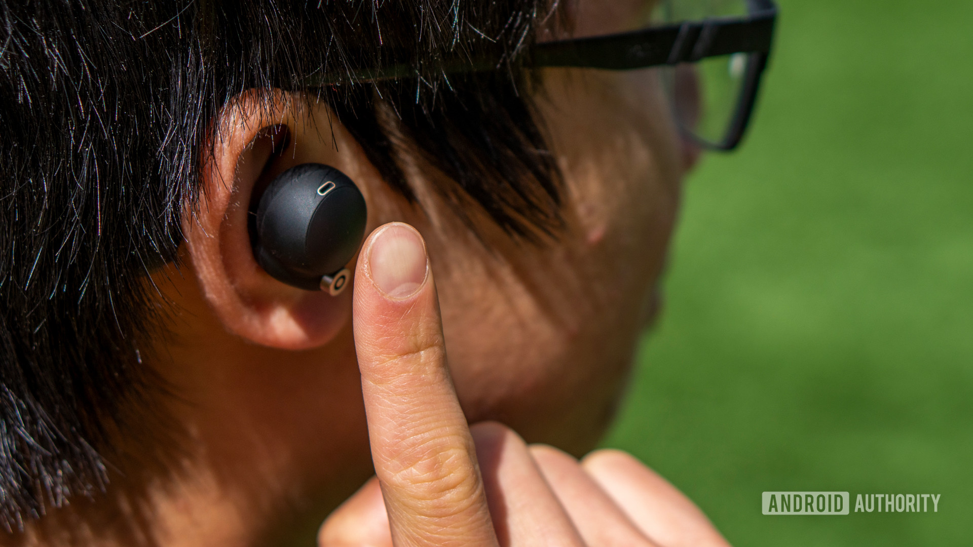 A woman putting her finger up to the Sony WF-1000XM4 earbud.