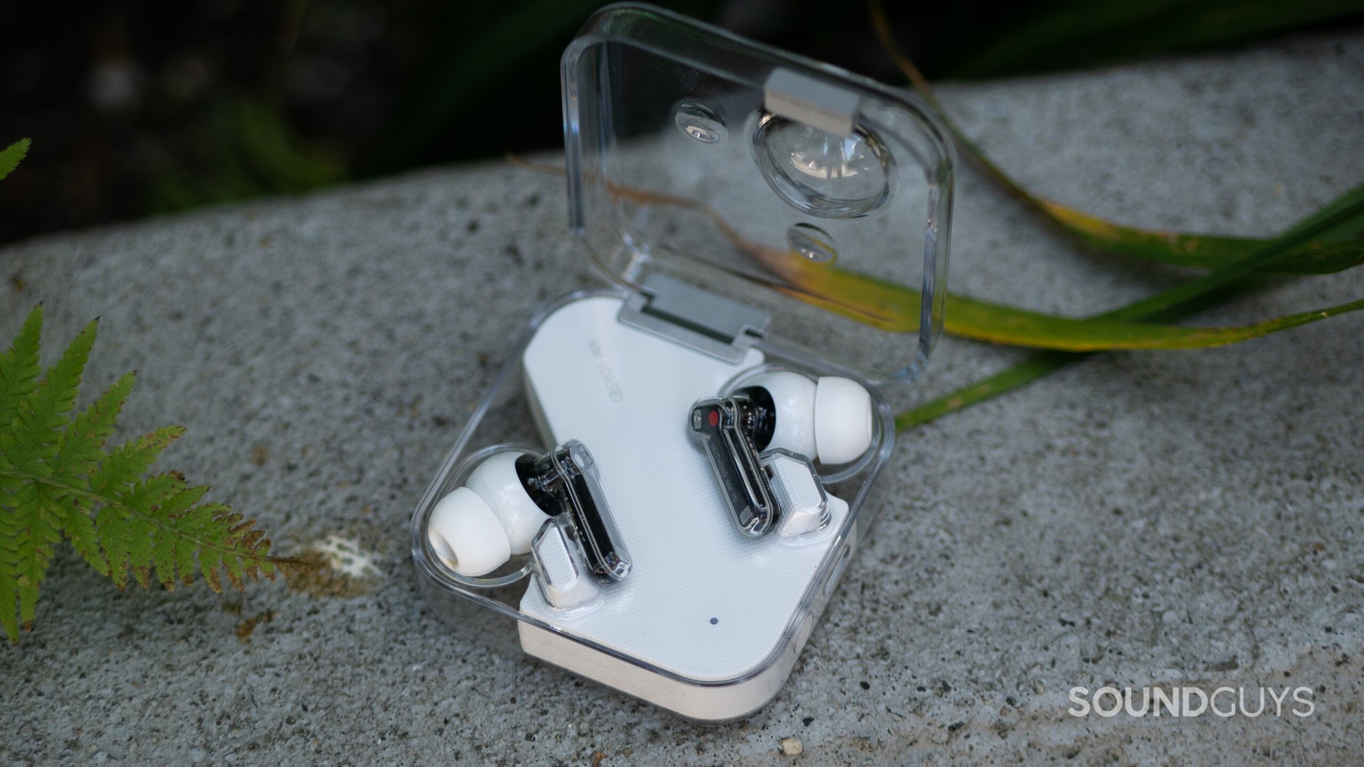 The Nothing Ear 1 lies on a concrete surface with the earbuds in the open case.