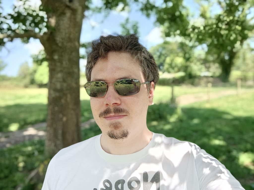 OnePlus Nord 2 5G camera sample selfie with bokeh of a man in a white t-shirt wearing shades, with brown hair and a brown beard.
