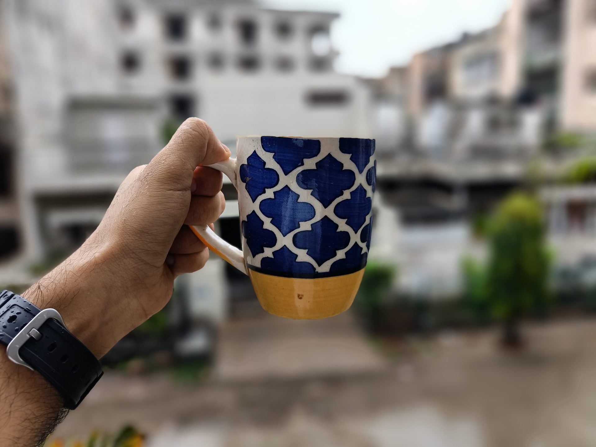 Poco F3 GT portrait mode from rear camera of hand holding a colorful blue, white, and yellow mug in front of a window.
