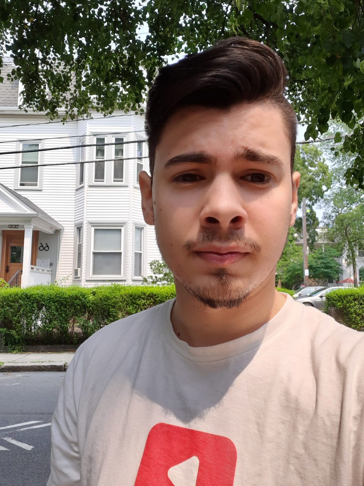 Samsung Galaxy XCover Pro Camera Samples selfie of a man with dark hair and a beard, wearing a light coloured t-shirt, with a white house behind him.