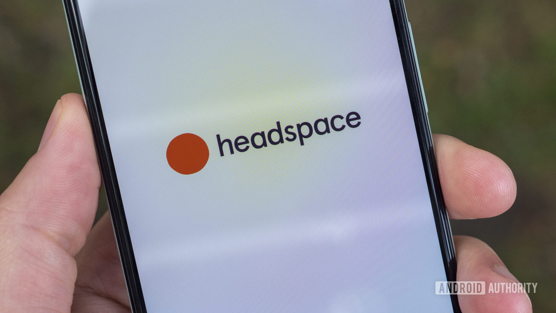 A user holds a smartphone in hand displaying the Headspace app logo.
