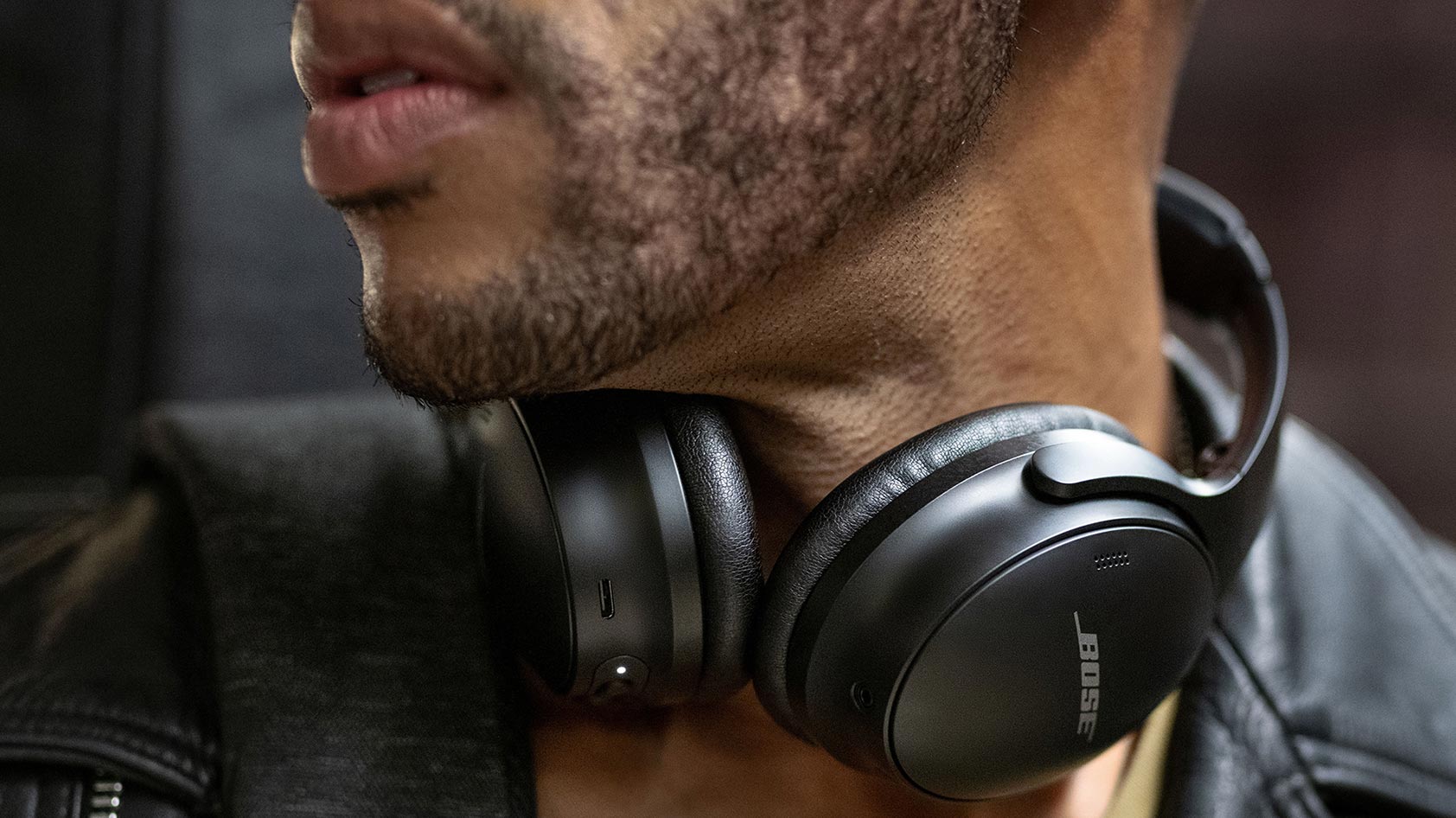 A man wears the Bose QuietComfort 45 noise-cancelling headphones in black around his neck.