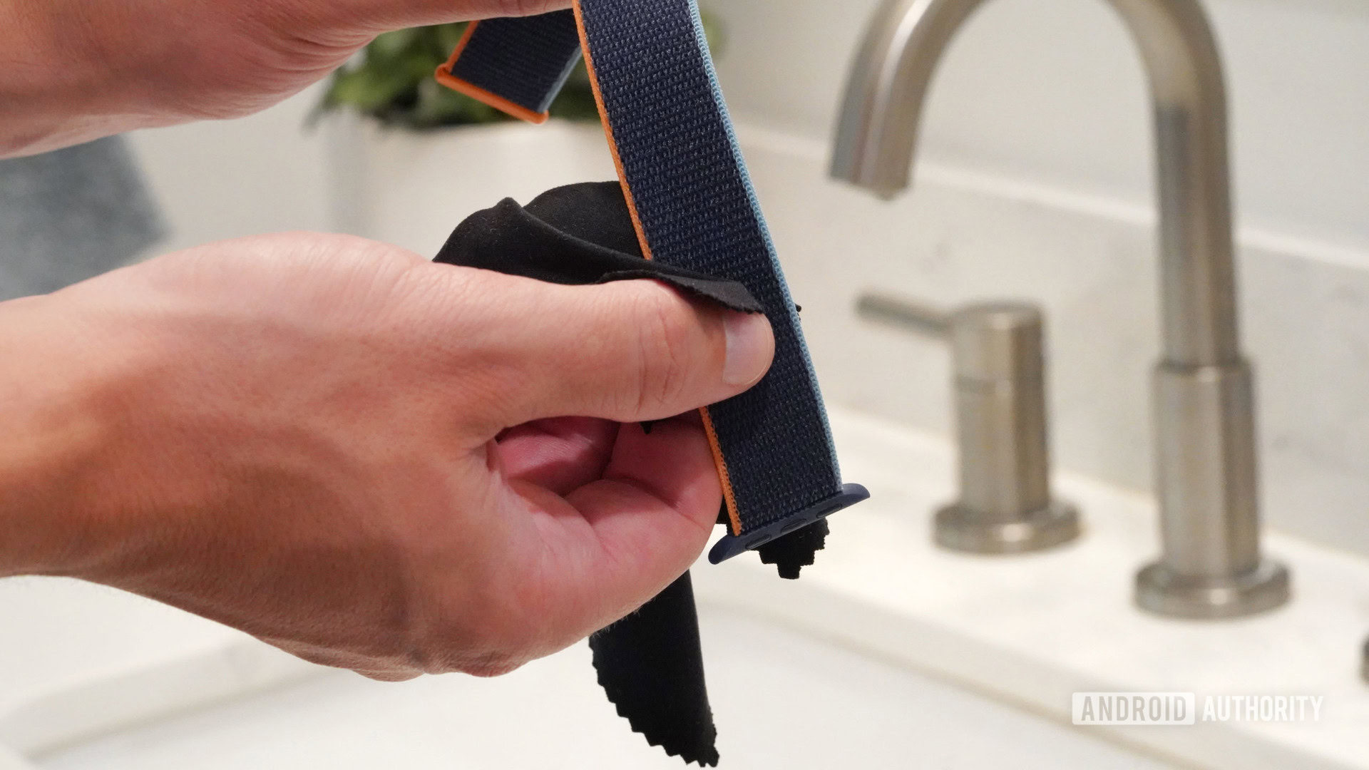 Men's hands clean the nylon Apple Watch band with a non-abrasive, lint-free cloth.