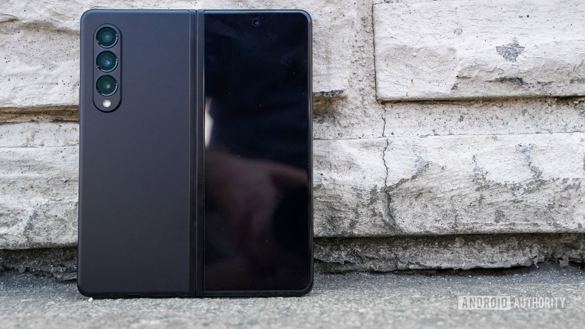 Vista trasera abierta del Samsung Galaxy Z Fold 3 que muestra el módulo de la cámara contra una pared de ladrillos.