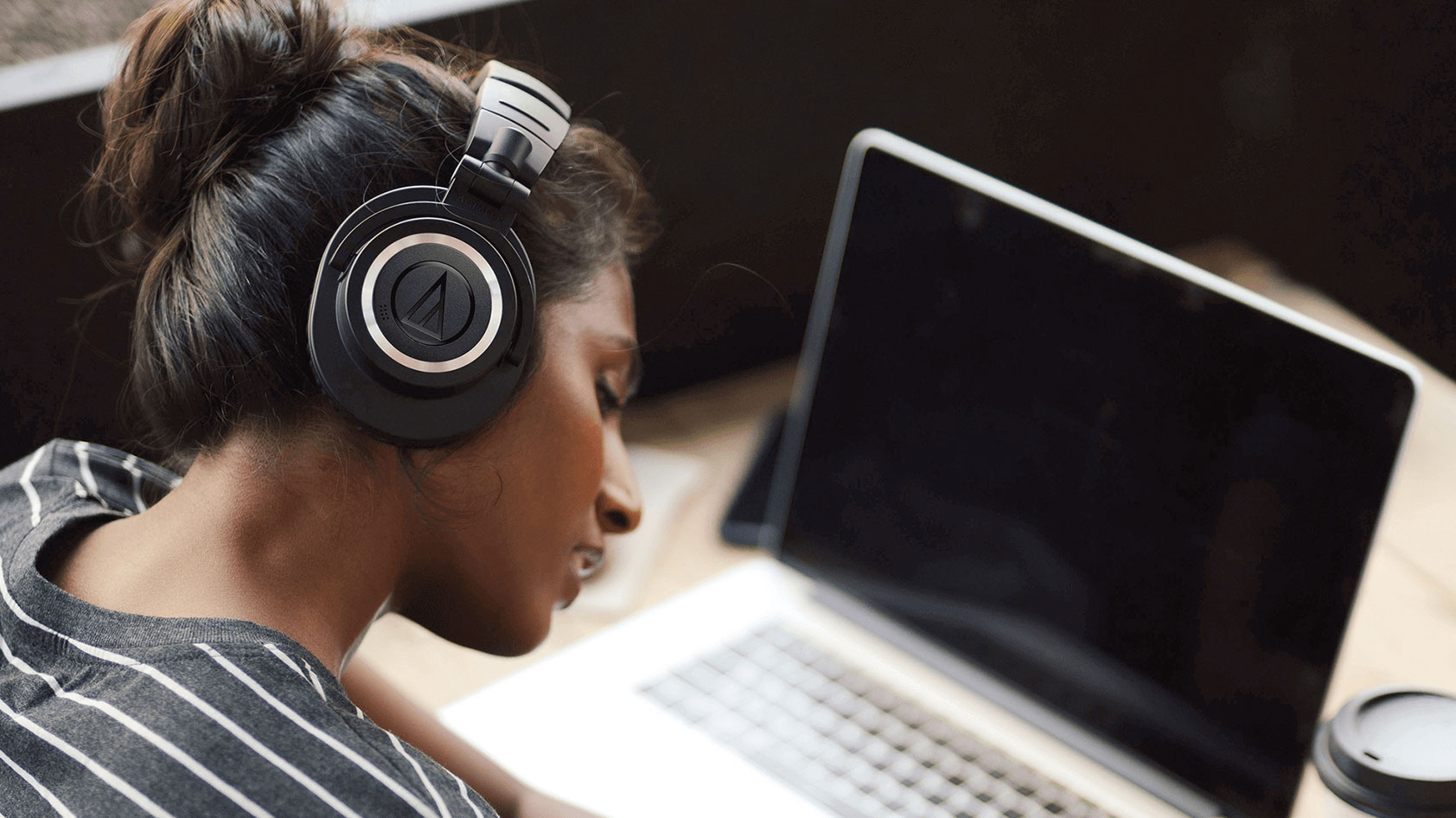 A woman wears the audio technica ath m50xbt2 wireless headphones in a coffee shop.