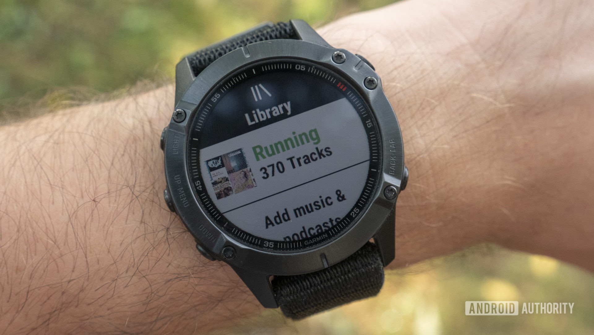 A Garmin Fenix 6 Pro on a user's wrist displays a running playlist in their Spotify music app.