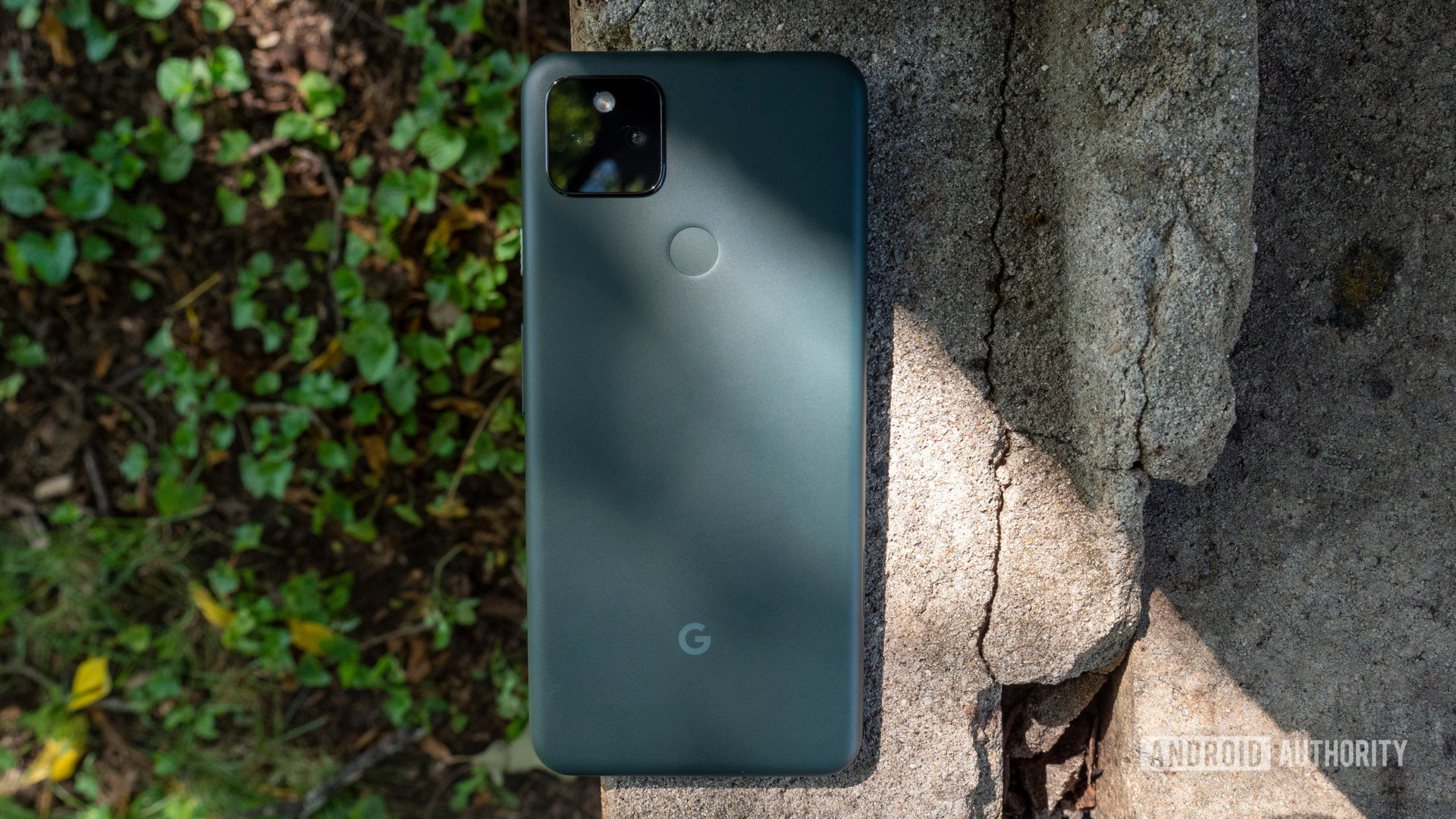 the google pixel 5a on a piece of cement showing its back in mostly black color