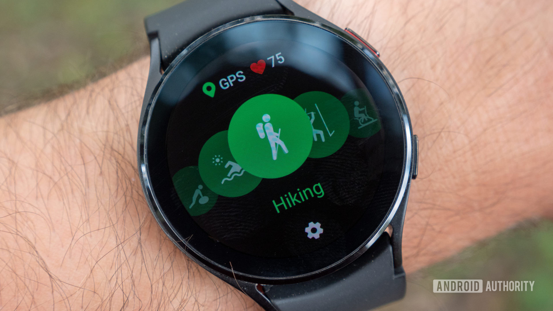 The Samsung Galaxy Watch 4 on a wrist showing the hiking workout mode with GPS and heart rate icons.