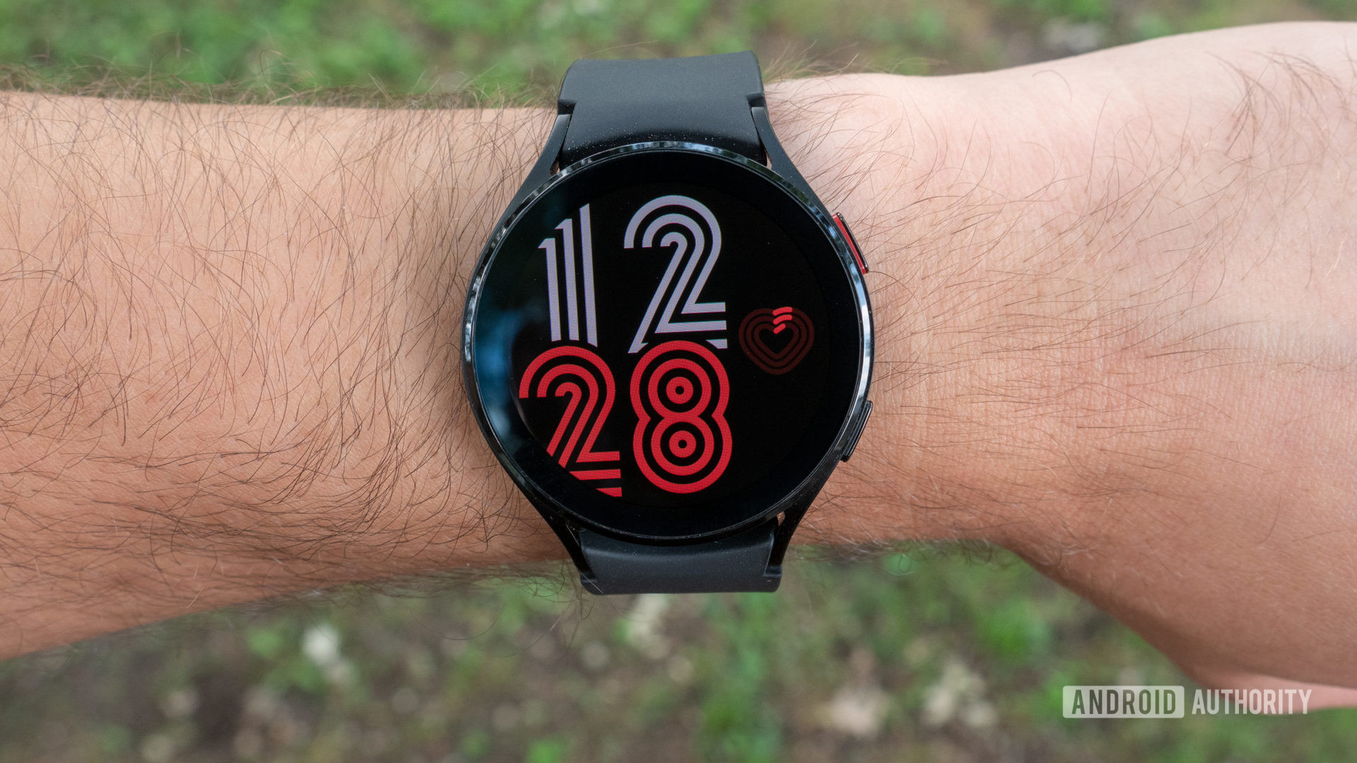 The Samsung Galaxy Watch 4 on a wrist displays a watch face with oversized numerals.