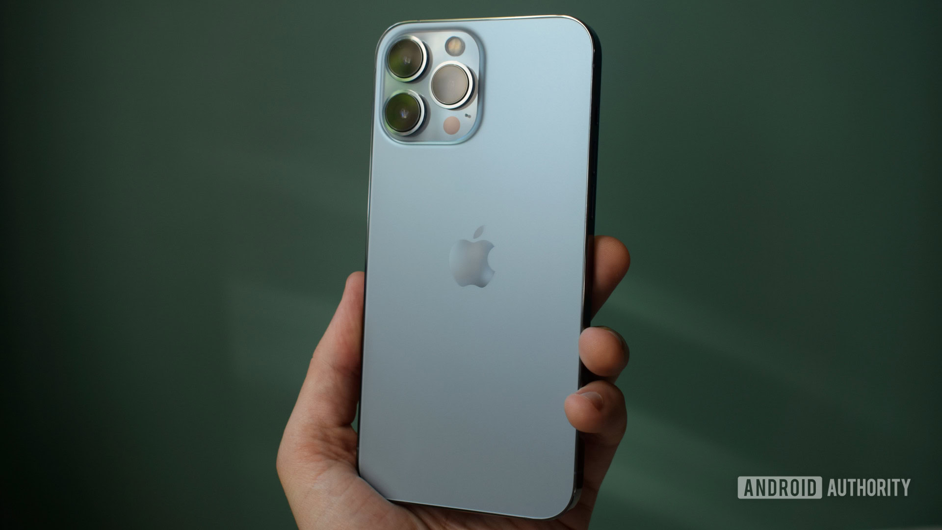 Apple iPhone 13 Pro Max nuevamente en la mano en la pared verde