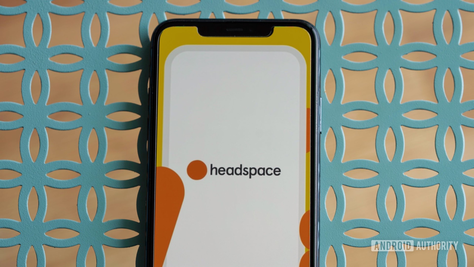 An iPhone 11 rests on a teal metal table, displaying the Headspace app logo.