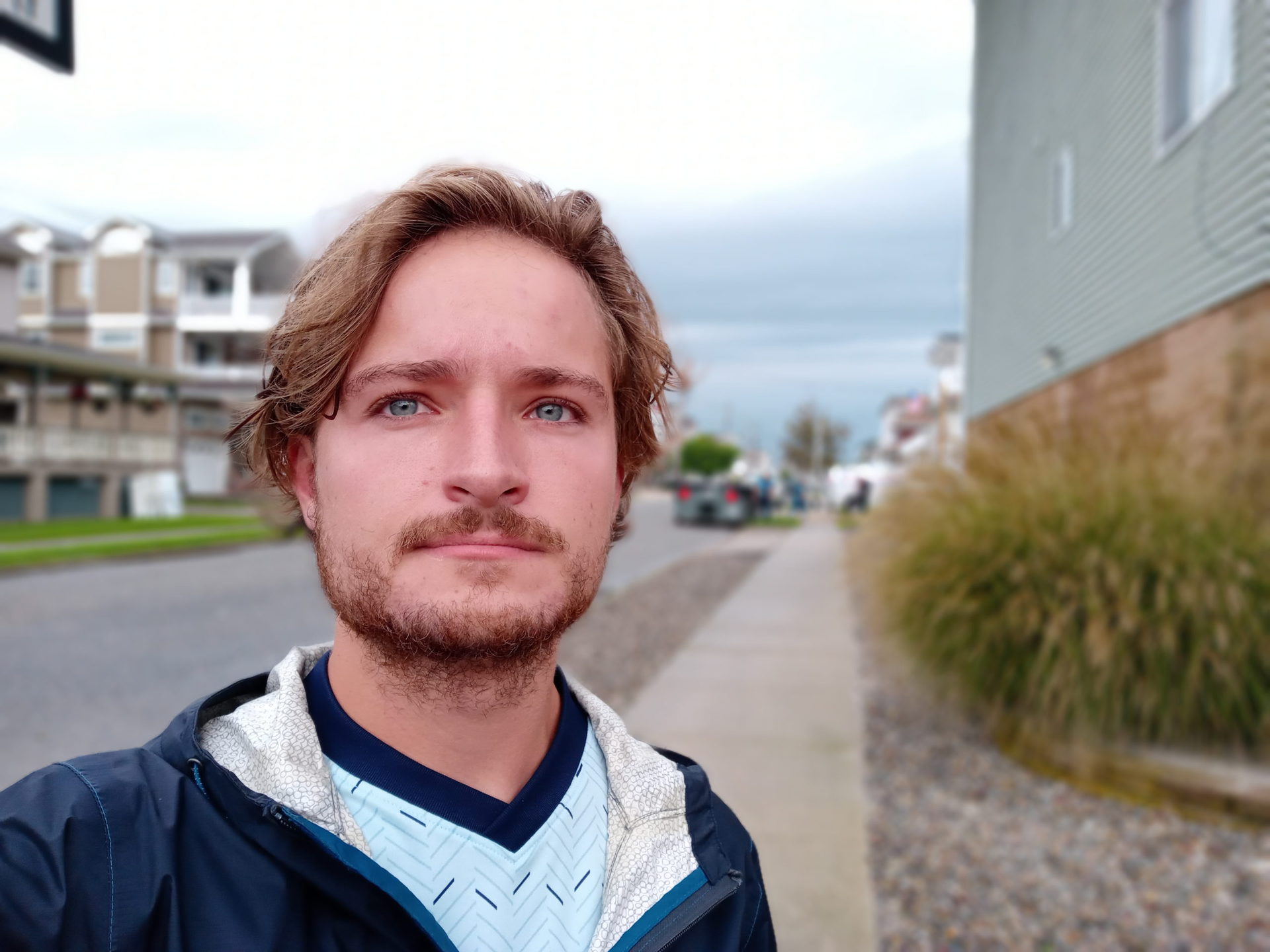 A portrait selfie taken with the LG K51 showing a man with light hair and facial hair wearing a white and blue t-shirt with a blue jacket over the top