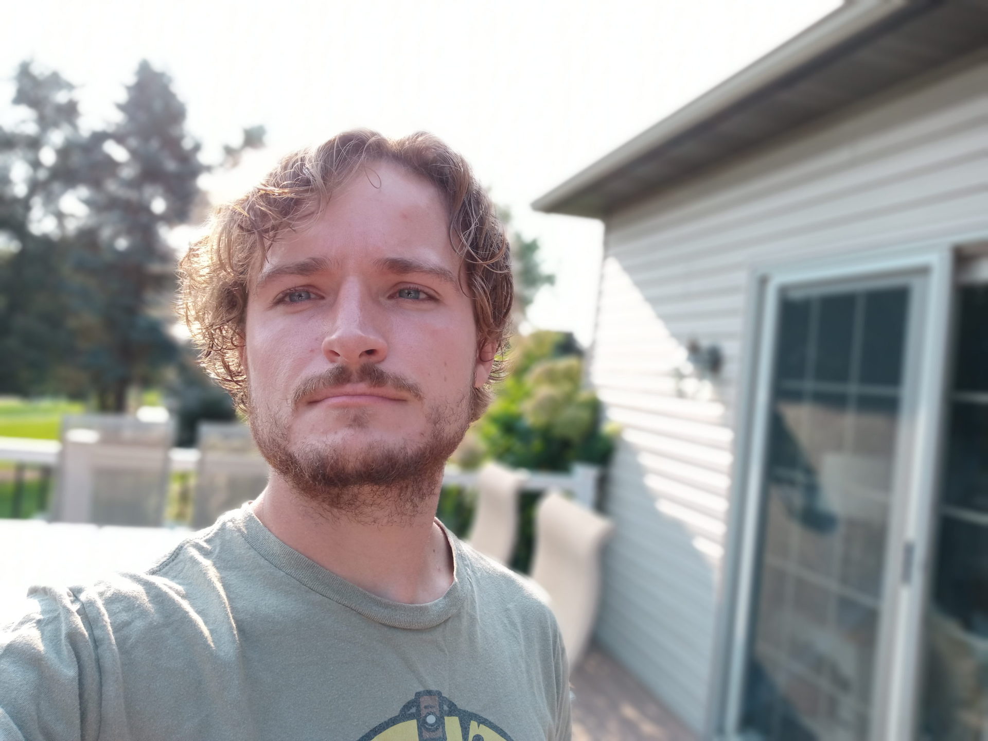 A portrait selfie taken with the LG Reflect of a man with light hair and facial hair wearing a grey t-shirt, taken outdoors.