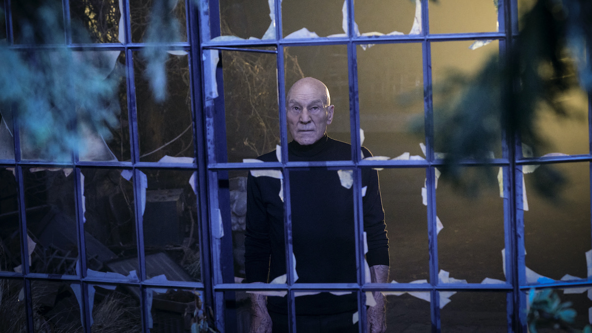 Patrick Stewart, as Jean-Luc Picard, looks out a broken window in Star Trek: Picard season 2