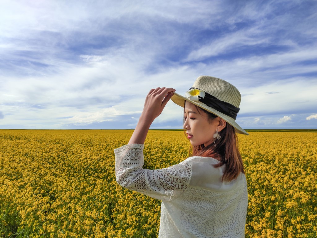 Picture of woman standing in a yellow field holding her hat