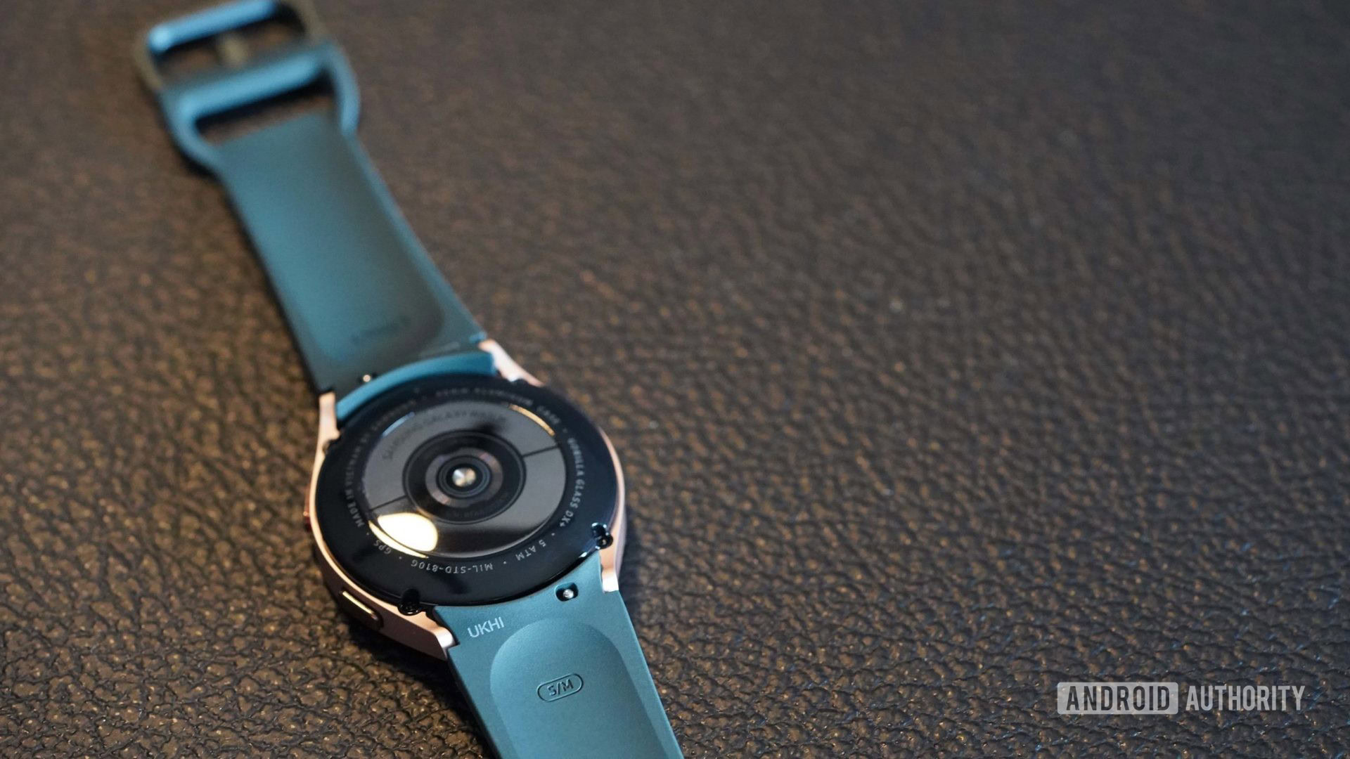 A Samsung Galaxy Watch 4 rests face down, exposing the band's spring bar.