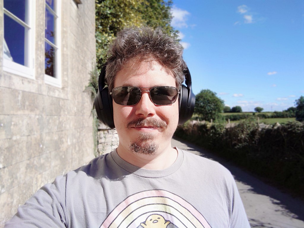 Sony Xperia 5 III camera sample selfie bokeh of a man with curly hair and a beard, wearing headphones and shades outdoors