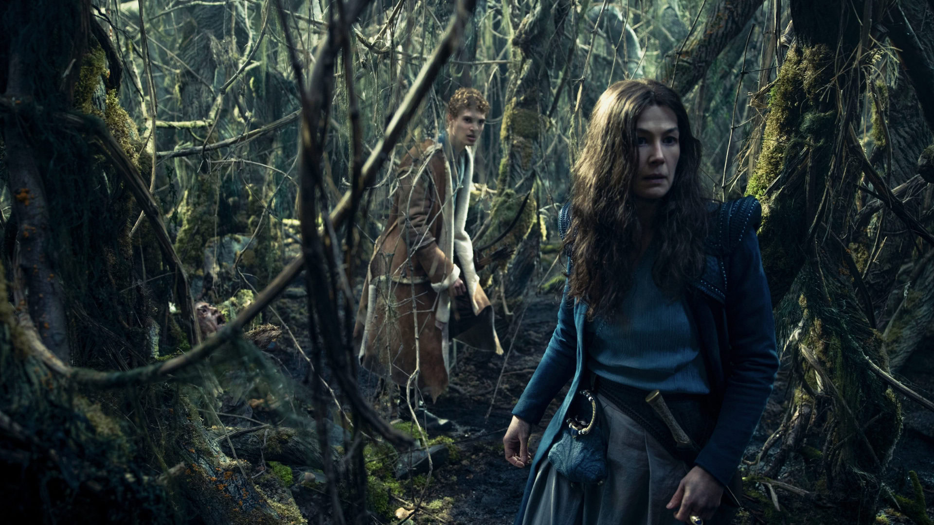 Rosamund Pike and Josha Stradowski walk through dense forest in The Wheel of Time 3 1