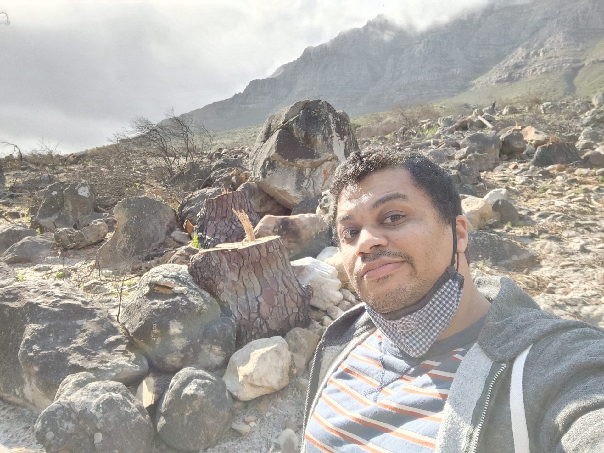 A vivo X70 Pro Plus selfie sample taken outdoors of a man with dark hair in a t-shirt and hoodie, with rocks behind him.