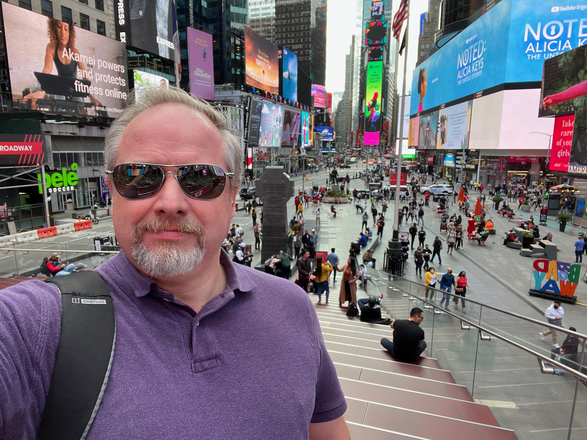 Apple iPhone 13 photo sample Times Square selfie of a man with light colored hair and beard wearing a purple top and black shades