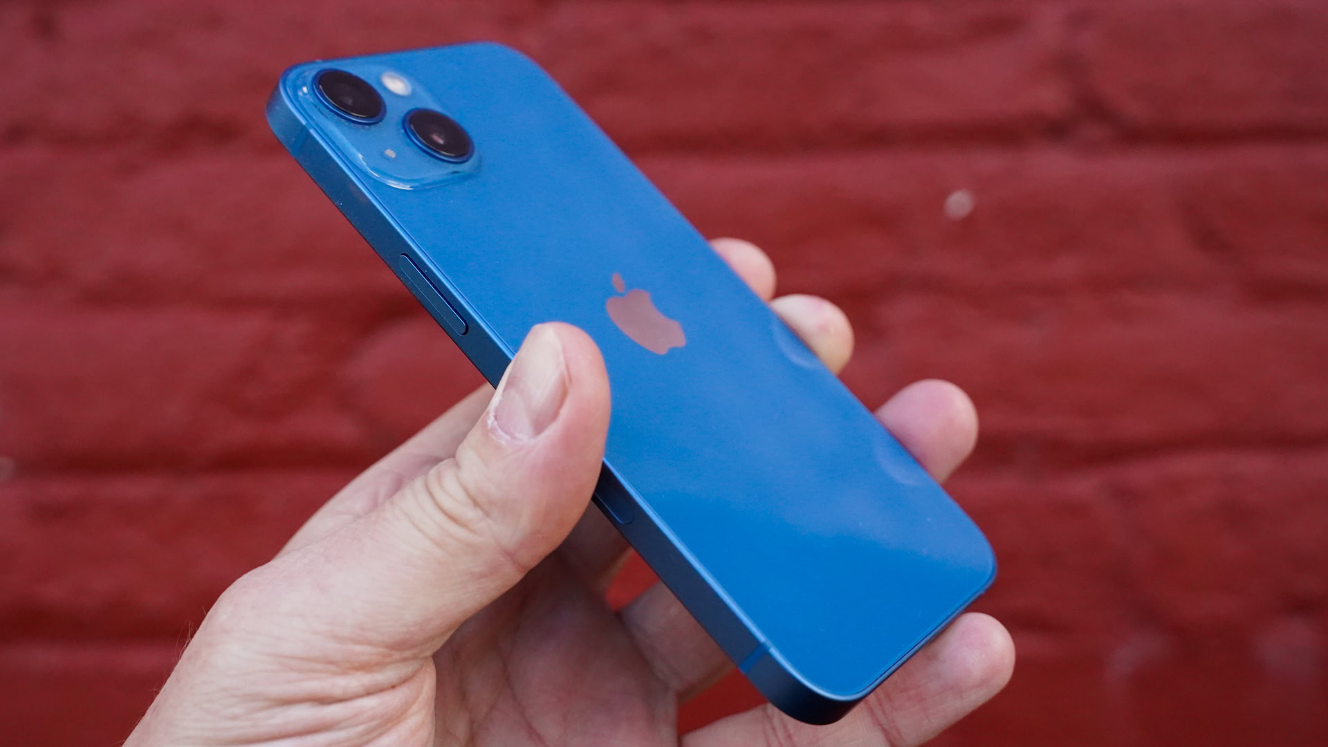 Perfil trasero izquierdo del Apple iPhone 13 contra una pared de ladrillos rojos