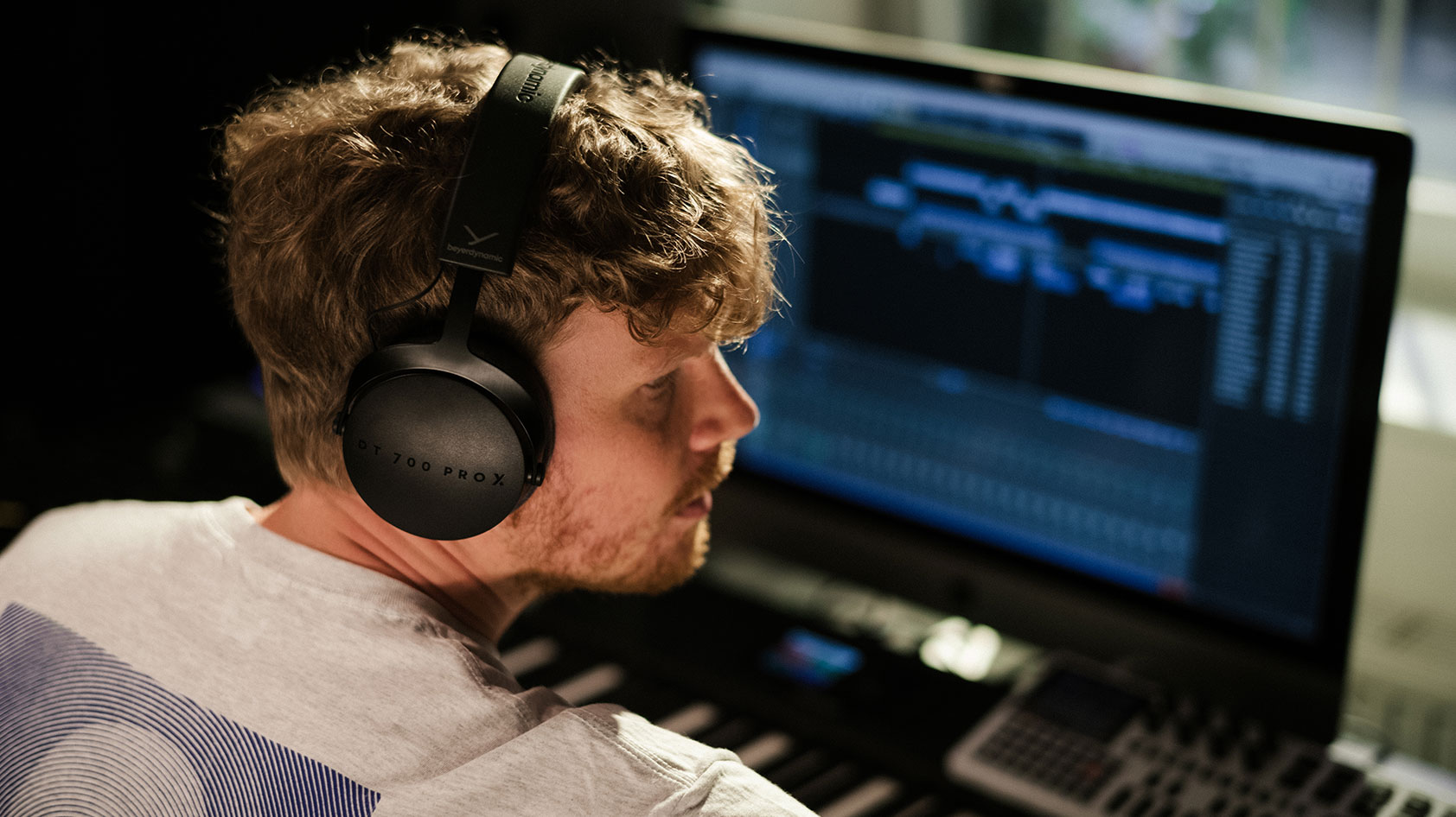 A masculine person wears the beyerdynamic DT 700 PRO X while mixing audio.