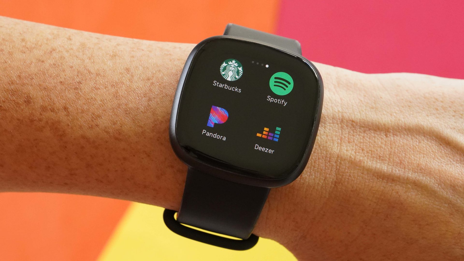 A Fitbit Versa 3 displays a number of apps stored on the device including Starbucks, Spotify, Deezer, and Pandora.