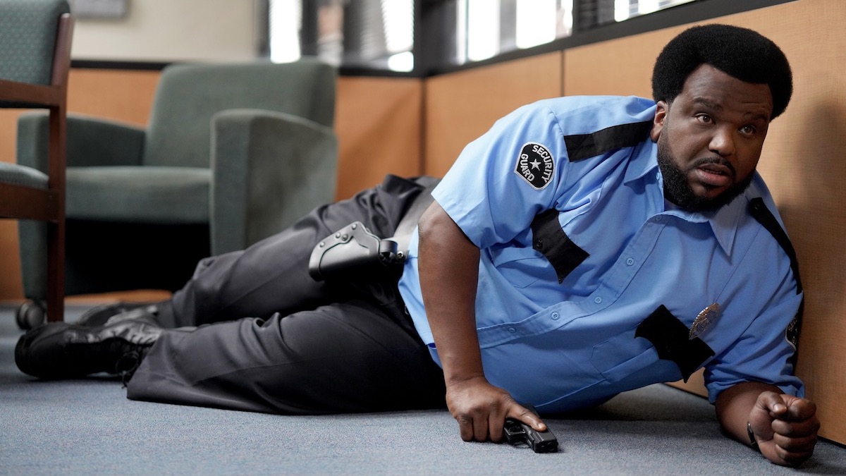 Craig Robinson as a security guard lying on the floor with a gun drawn in Killing it - best peacock originals