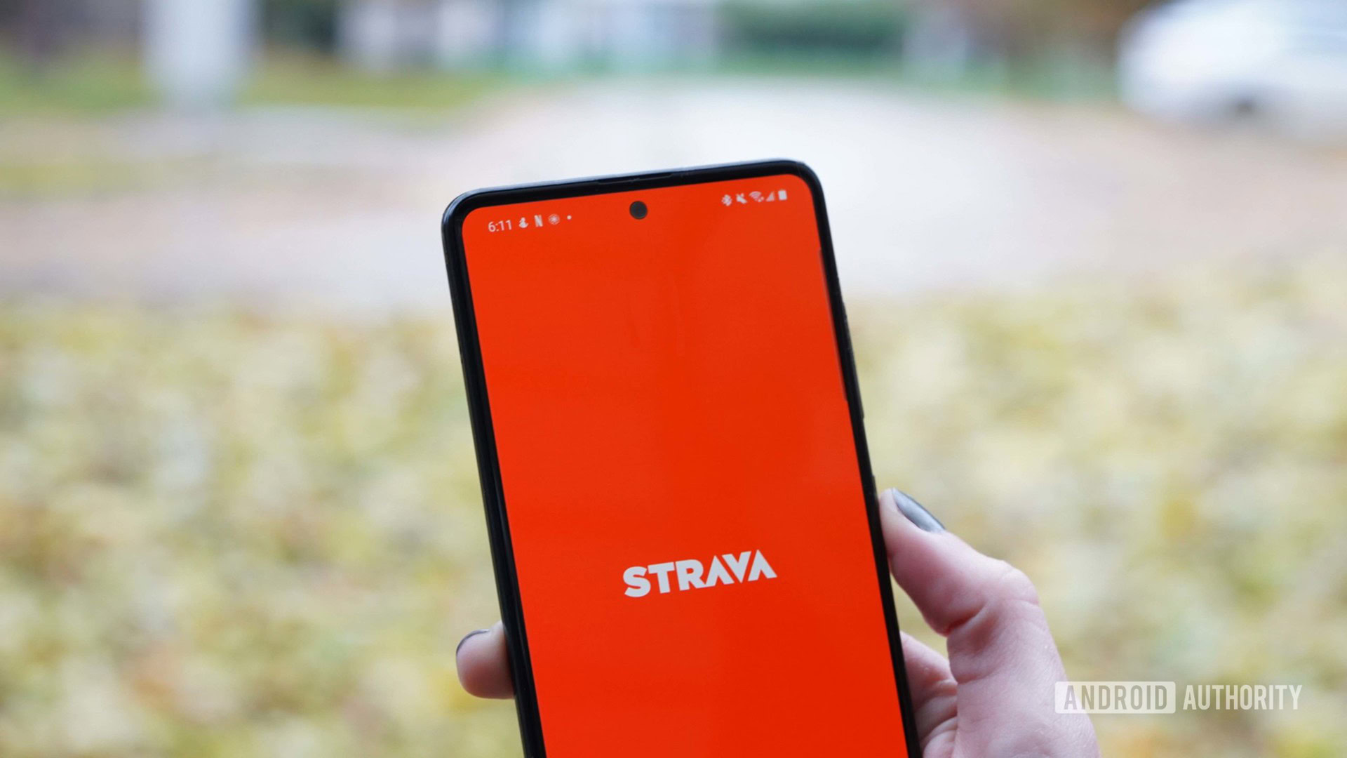 The Strava fitness app home screen is displayed on a Samsung Galaxy A51 on a leaf strewn street.