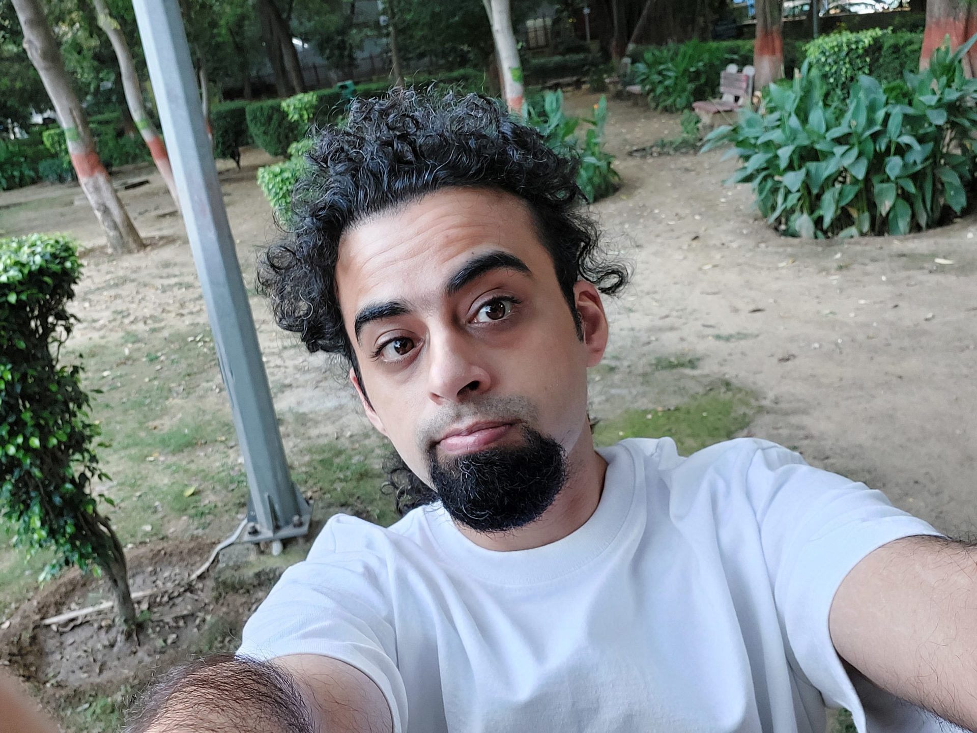 Samsung Galaxy M52 camera sample selfie normal of a man with dark curly hair and a beard wearing a white t-shirt outdoors