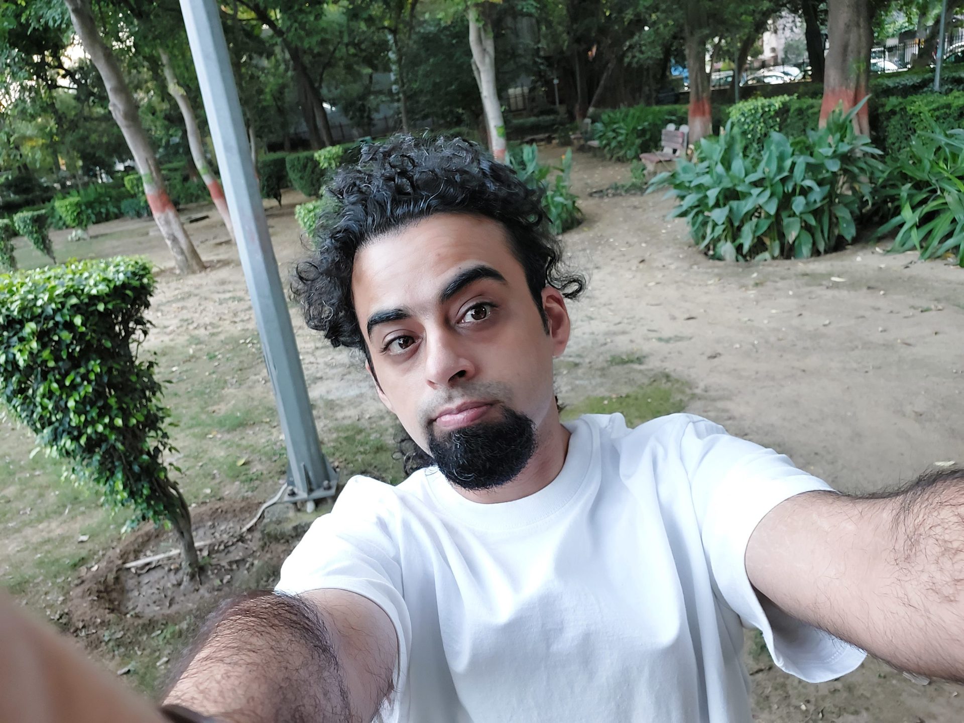 Samsung Galaxy M52 camera sample selfie ultra wide of a man with dark curly hair and a beard wearing a white t-shirt outdoors