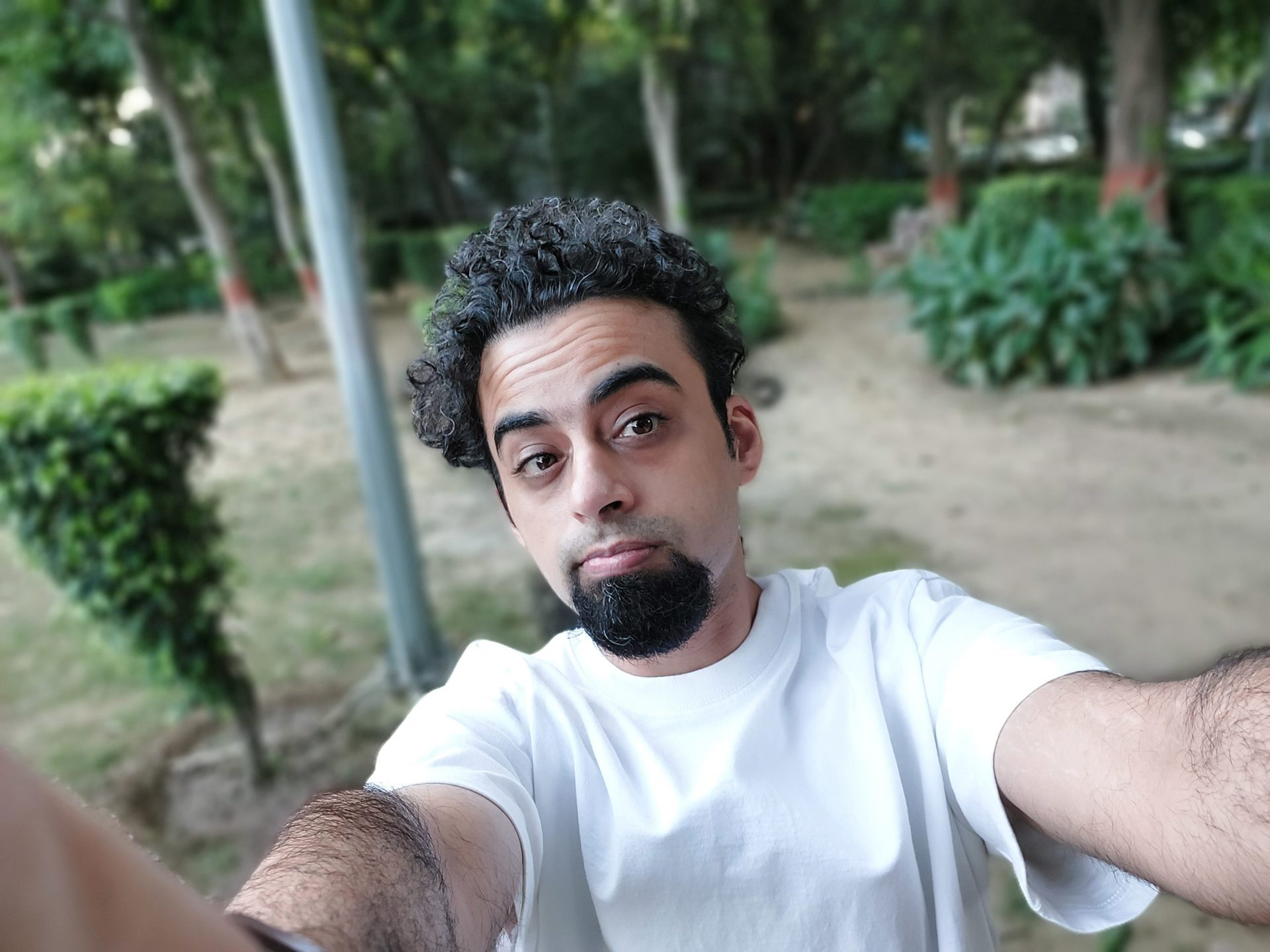 Samsung Galaxy M52 camera sample selfie ultrawide portrait of a man with dark curly hair and a beard wearing a white t-shirt outdoors