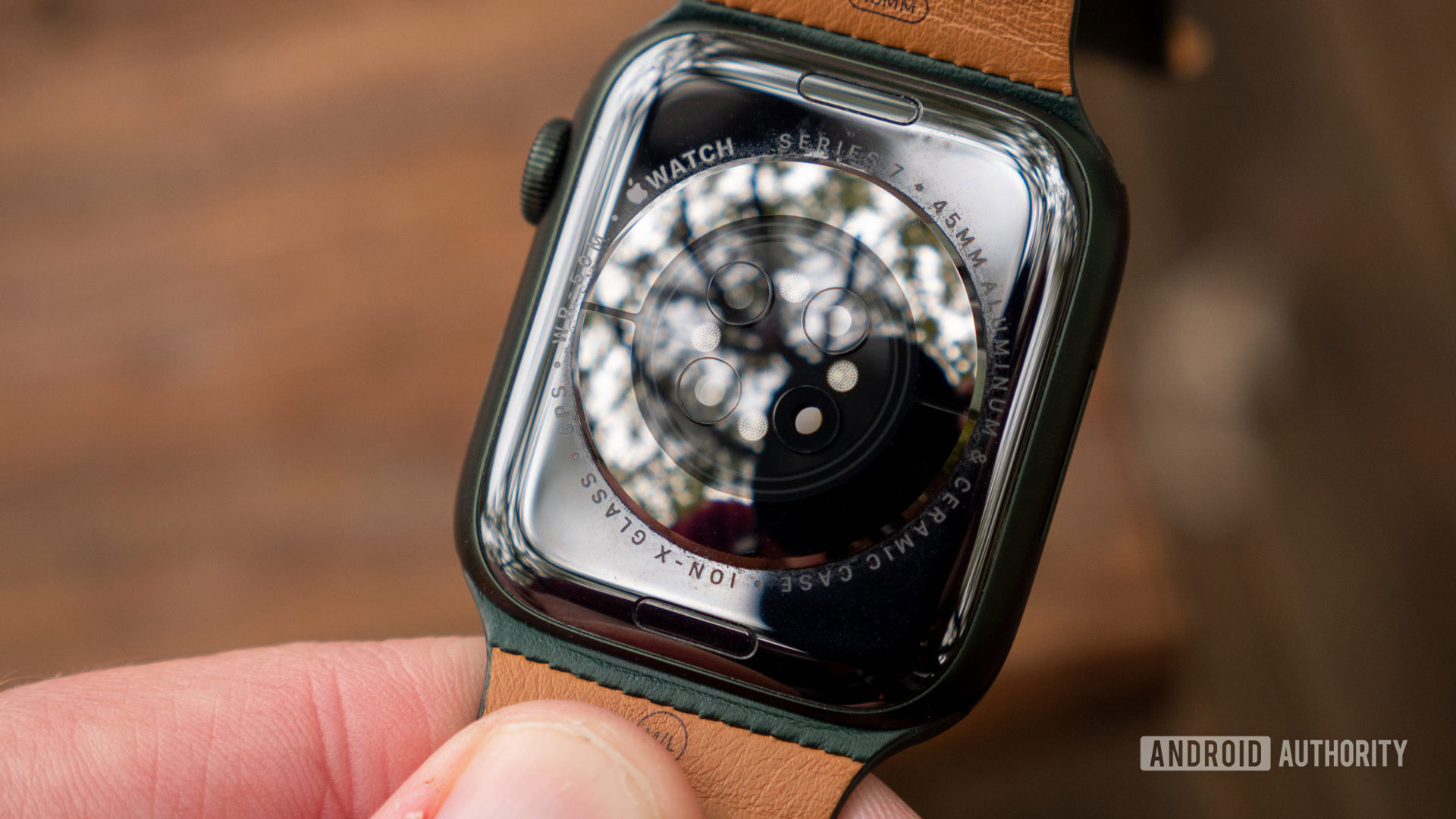 A user holds an Apple wearable face down, showcasing the device's heart rate sensor.