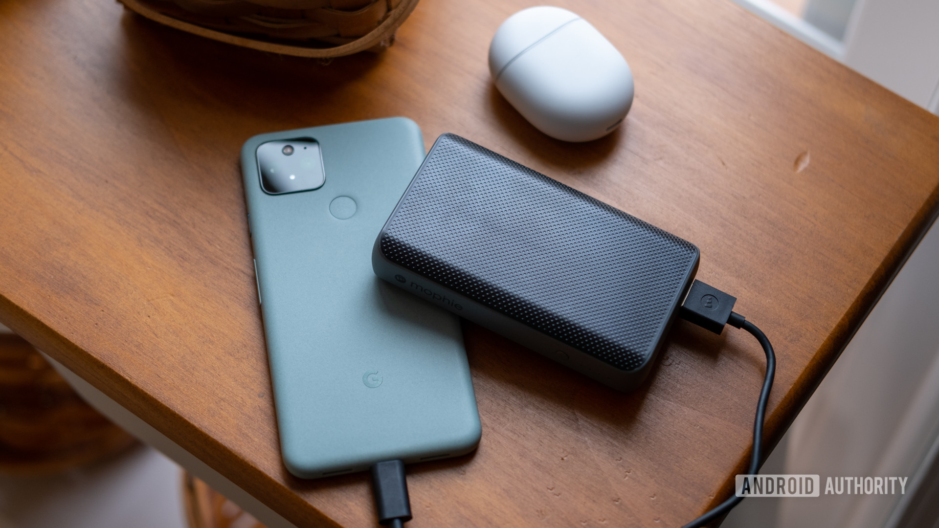 The Mophie PowerStation PD XL on a table charging a Pixel 5 and next to Pixel Buds.