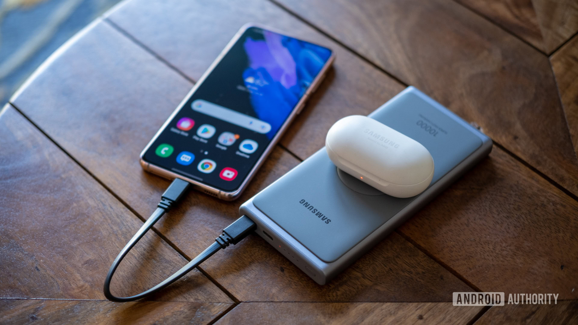 Samsung super fast power bank on table charging S21 and Galaxy Buds above