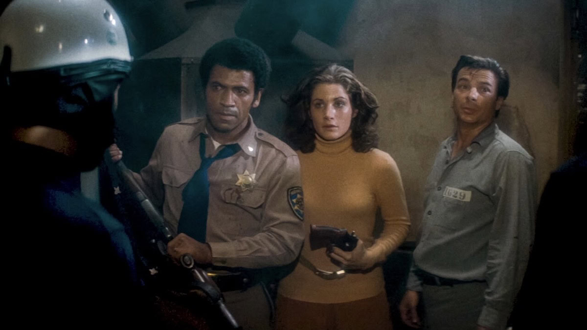 Three people stand with their backs to the wall, armed, in Assault on Precinct 13 - best showtime movies