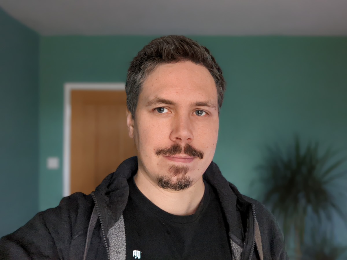 Camera sample selfie indoor portrait of a man with dark hair wearing a black t-shirt and hoodie, taken on the Google Pixel 6 Pro