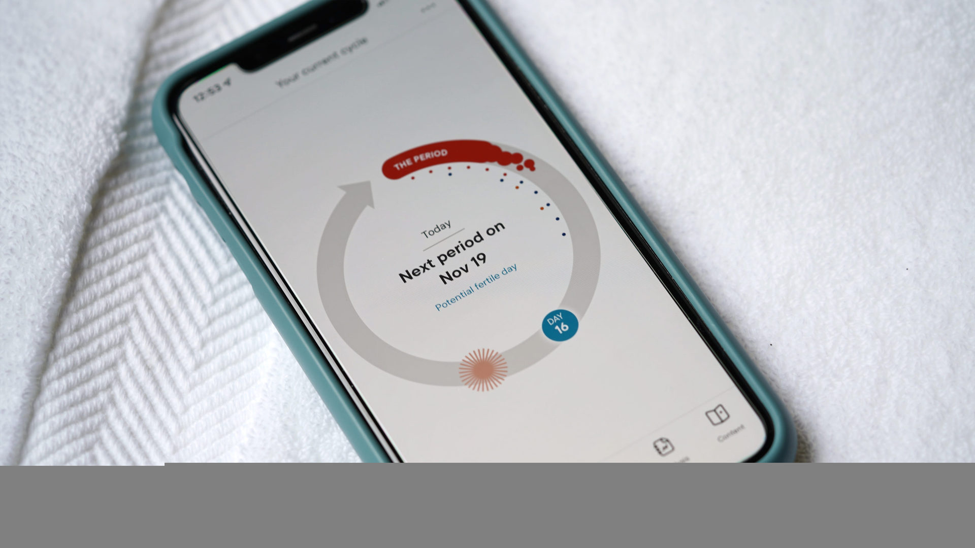 An iPhone 11 rests on white towels display the Clue period and ovulation tracker app.