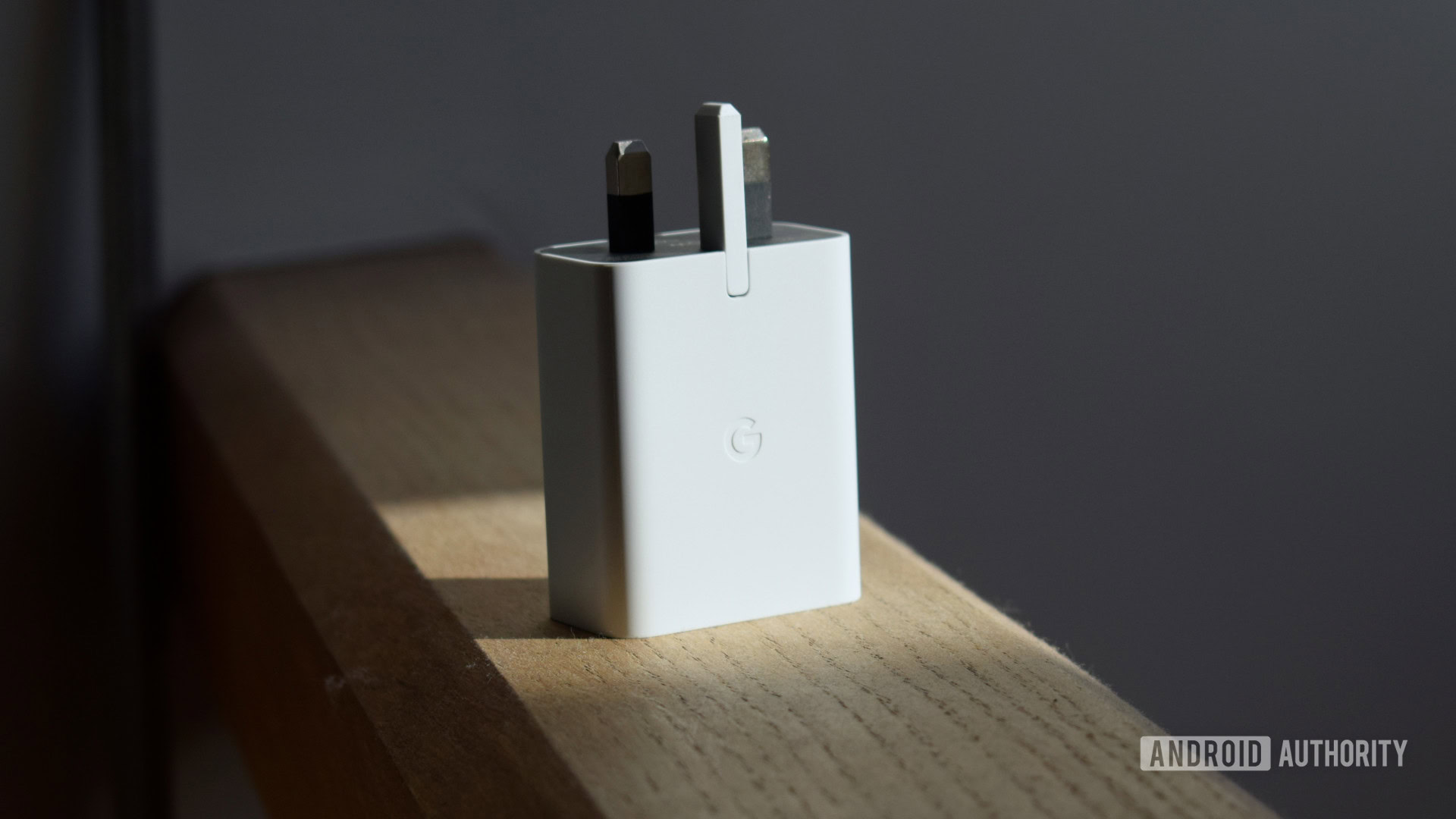 Захранващ адаптер Google 30 W USB-C, стоящ изправен върху дървена греда