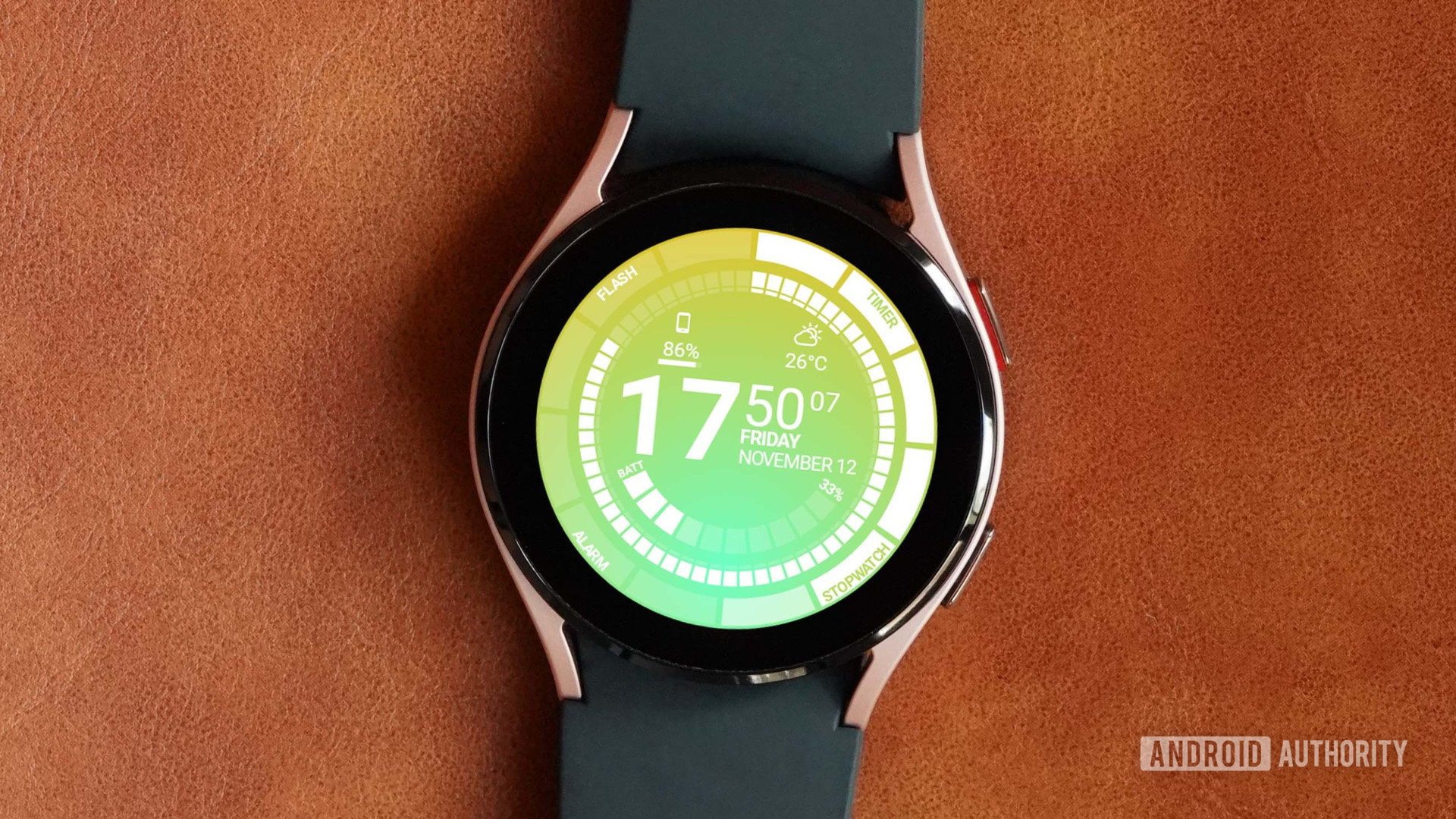 A Samsung Galaxy Watch 4 rests on a leather surface displaying the watch face Venom by Thema.
