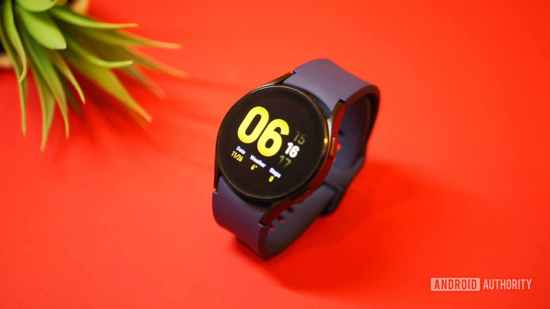 Samsung Galaxy Watch 4 sobre fondo rojo, mostrando el reloj de la pantalla de inicio