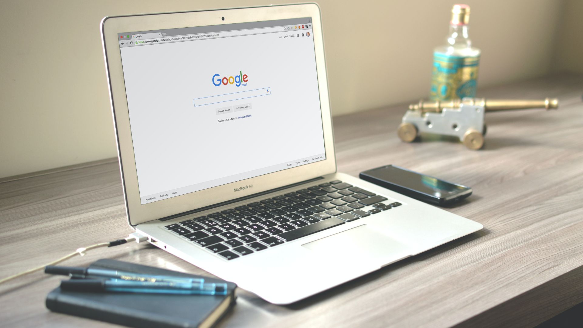 MacBook Air running Google Chrome sitting on desk with a black phone to its right and a notebook with pens to its left.