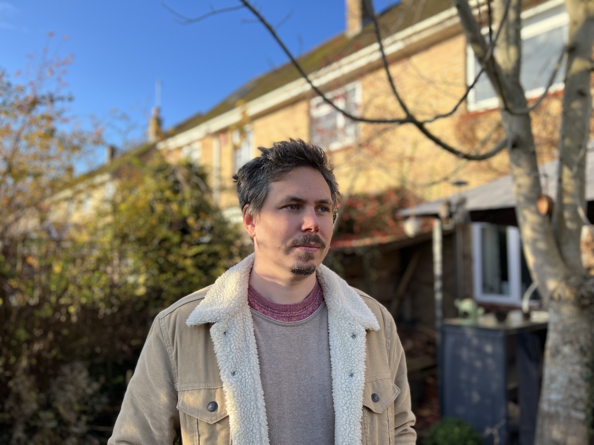 Portrait of man standing outdoors in front of brick house shot on Apple iPhone 13 Pro Max